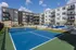 Modern apartment complex featuring a vibrant blue tennis court and luxurious poolside lounging area under a clear sky.