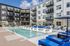 Modern apartment complex featuring a refreshing outdoor pool with stylish loungers and sun umbrellas, surrounded by contemporary multi-story buildings.