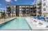 Modern apartment complex with a vibrant outdoor swimming pool, surrounded by stylish lounge chairs and contemporary architecture under a clear blue sky.