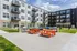 Contemporary apartment complex with vibrant outdoor seating, BBQ area, and stylish balconies under a blue sky.