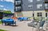 Inviting outdoor patio area at modern apartment complex featuring vibrant blue seating, sleek tables, and a convenient barbecue grill under a bright blue sky.