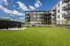 Modern apartment complex with spacious balconies and a lush green courtyard under a bright blue sky.