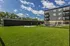 Modern apartment building with balconies overlooking a lush green lawn and a sunny courtyard, offering a serene living environment.