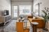 Bright and modern living room with a cozy mustard sofa, stylish armchair, and sleek entertainment center, enhanced by large windows and natural light.