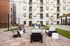 Modern apartment building with a stylish outdoor patio featuring comfortable seating, a sleek fire pit, and ambient string lighting, perfect for social gatherings.