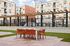 Modern outdoor seating area with vibrant orange chairs and a sleek white table under decorative string lights, surrounded by contemporary apartment buildings.
