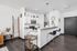 Modern open-concept kitchen with sleek white cabinetry, stainless steel appliances, and a stylish breakfast bar with chic bar stools. Warm wood flooring complements the contemporary design.