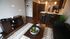 Modern apartment living room with sleek dark wood flooring, stylish black leather sofa, and a contemporary kitchen featuring an open breakfast bar with chic bar stools.