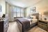 Bright and cozy bedroom featuring a rustic wooden bed frame, elegant decor, and large sunlit windows.
