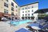 Luxurious apartment complex featuring a stylish outdoor pool area with comfortable lounge chairs, cabanas, and vibrant umbrellas under a clear blue sky.