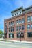 Charming brick apartment building with large windows, vibrant flower baskets, and a welcoming leasing office entrance.