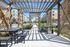 Charming outdoor pergola with modern seating, surrounded by lush greenery and adjacent to stylish apartments.