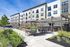 Modern apartment building with stylish patio, featuring outdoor seating, umbrellas, and lush landscaping under a clear blue sky.