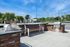 Charming outdoor patio with a sleek stainless steel grill, brick counters, and a stylish bench under a vibrant blue sky.