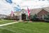 Charming brick apartment complex with lush landscaping and welcoming flags under a bright blue sky.