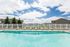 Inviting outdoor pool area with crystal-clear water, surrounded by sun loungers and a charming white picket fence, set against a backdrop of lush greenery and blue skies.