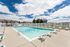 Inviting outdoor swimming pool area with ample lounge chairs, surrounded by a charming residential community under a bright, blue sky.