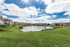 Scenic apartment community with charming buildings overlooking a tranquil pond and lush green lawns under a vibrant blue sky.