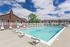 Inviting apartment complex with a sparkling outdoor pool surrounded by modern lounge chairs and charming brick architecture.