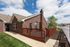 Charming brick home with a spacious wooden deck, surrounded by lush greenery and a serene neighborhood backdrop.