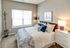 Cozy bedroom with modern decor, featuring a plush bed with colorful pillows, a stylish lamp, and a sunny window view.