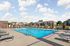 Inviting outdoor pool area with comfortable lounge chairs, surrounded by charming brick architecture and lush green landscaping.