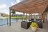 Charming outdoor seating area under a wooden pergola overlooking a serene pond view with fountain, featuring stylish wicker furniture and lush greenery.