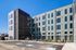 Modern apartment building exterior with sleek design, large windows, and accessible parking spaces under a clear blue sky.