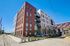 Modern urban apartment complex featuring sleek brick and white panel facade, large windows, and inviting greenery set against a clear blue sky.