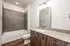 Elegant bathroom featuring a sleek granite countertop, modern lighting, and a stylish tiled bathtub.