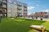 Vibrant apartment courtyard featuring lush green lawn, hammocks, and relaxing seating areas under a clear blue sky.