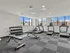 Modern apartment gym with large windows, featuring treadmills, exercise bikes, and free weight station, offering a bright and motivating workout space.