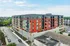 Modern urban apartment building featuring vibrant red and gray facade, surrounded by greenery and ample parking space.