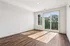 Bright and modern empty room with elegant wood flooring, large sliding glass doors opening to a balcony with lush green views.