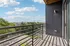 Charming balcony with sleek railing, offering panoramic views of lush greenery and a bright blue sky.