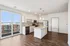 Modern apartment with a sleek kitchen featuring stainless steel appliances and granite countertops, complemented by a balcony view and hardwood floors.
