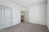 Bright and spacious bedroom with plush carpet and modern doors, leading to a glimpse of a stylish kitchen with warm lighting.