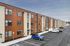Modern apartment building with a sleek wood and brick exterior, featuring large windows and ample parking space in a contemporary setting.
