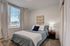 Cozy and bright bedroom with plush carpeting, featuring a large window with elegant drapes and a stylish bed setup.