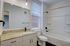 Modern bathroom with granite countertop, sleek sink, and large mirror, featuring a full bathtub and bright window with blinds.
