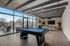 Modern entertainment room with pool table, cozy seating, and ample natural light from large windows overlooking a scenic view.