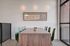 Chic dining area featuring a stylish wooden table, modern green chairs, and artistic wall decor, illuminated by elegant lighting.