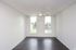 Bright and airy room with sleek dark hardwood floors, large windows, and a modern ceiling fan.