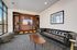 Modern living area with a sleek black leather sofa, wooden shelving unit displaying decor and books, large window with natural light, and a stylish coffee table.