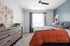 Modern bedroom with cozy orange bedding, stylish wooden dresser, and elegant wall art, bathed in natural light from large window.