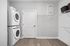 Contemporary laundry room with stacked washer and dryer, sleek open shelving, and elegant wood flooring.