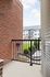 Charming patio space with elegant brick wall and modern railing, offering a serene view of well-maintained gardens and stylish neighboring buildings.