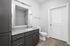 Modern bathroom with sleek dark cabinetry and granite countertop, complemented by a chic tiled shower and elegant flooring.