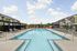 Inviting residential apartment complex with a luxurious outdoor pool, surrounded by stylish lounge chairs and shaded cabanas, offering a perfect spot for relaxation.