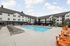 Modern apartment complex featuring a pristine outdoor swimming pool with ample lounge chairs, surrounded by stylish multi-story buildings under a bright, blue sky.